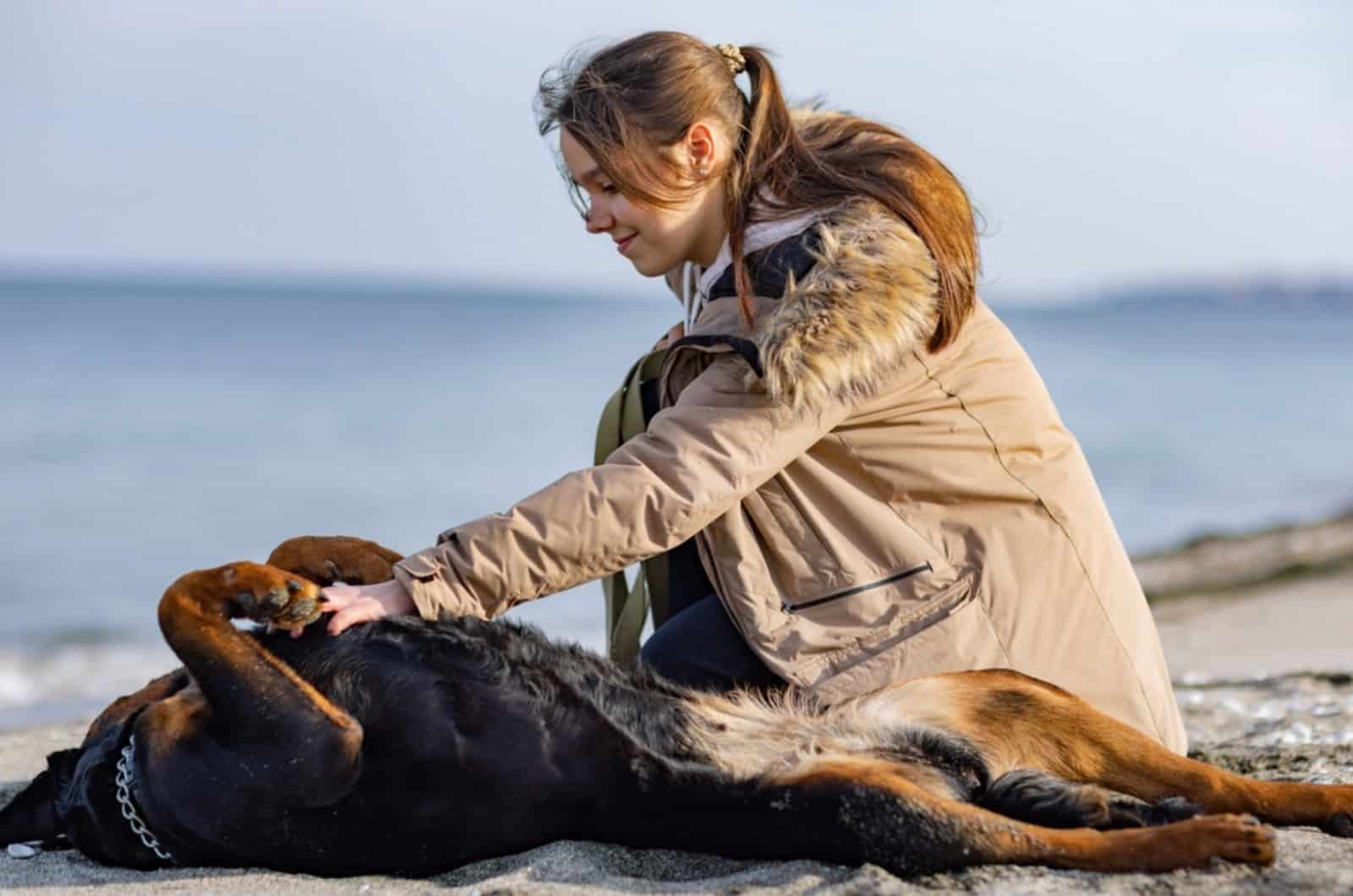 a girl cuddling her rottweiler on the beach