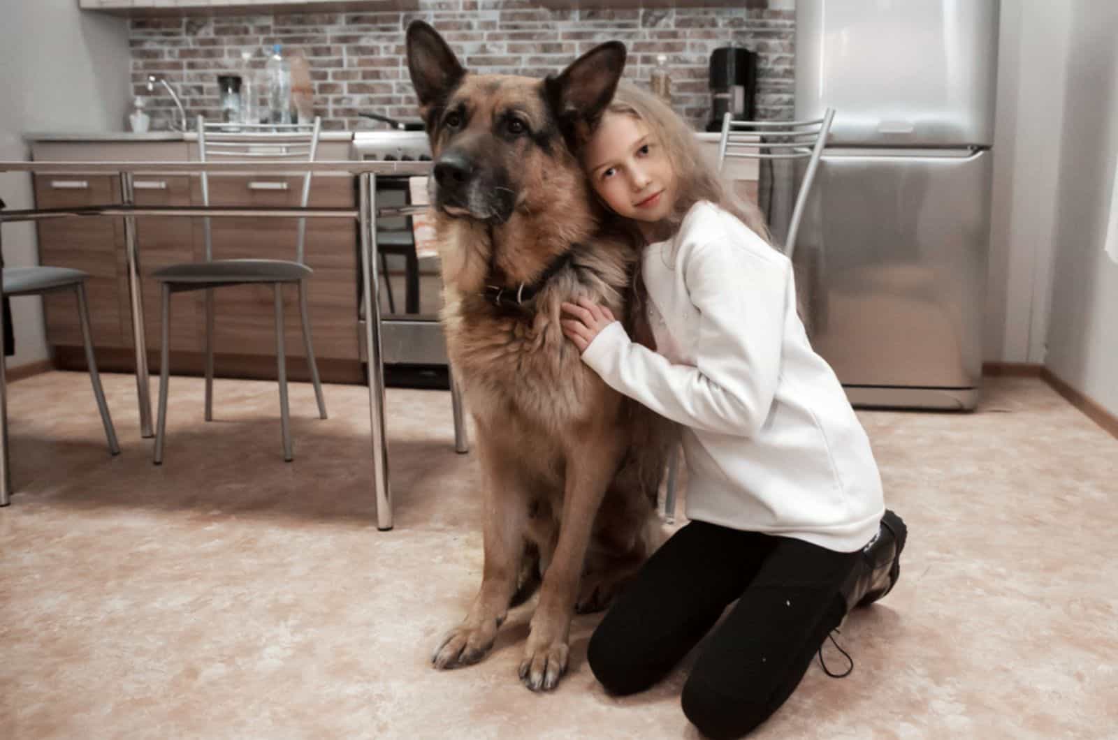 a girl hugging her pet german shepherd in the kitchen