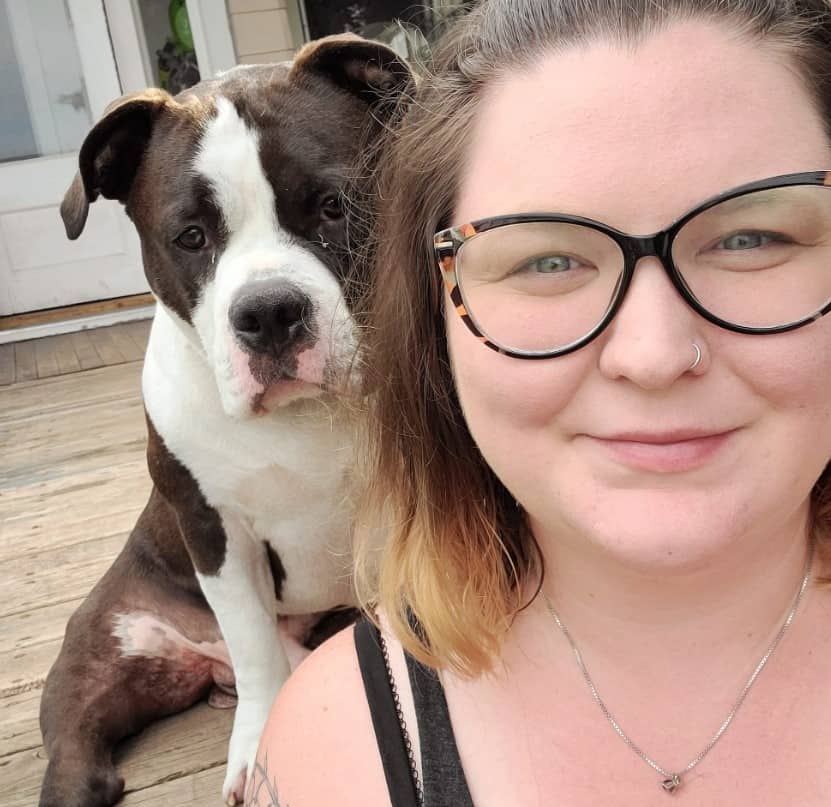 a girl with glasses takes a picture with a posing dog