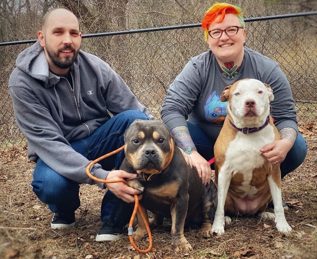 a man and a woman take a picture with their two adopted puppies