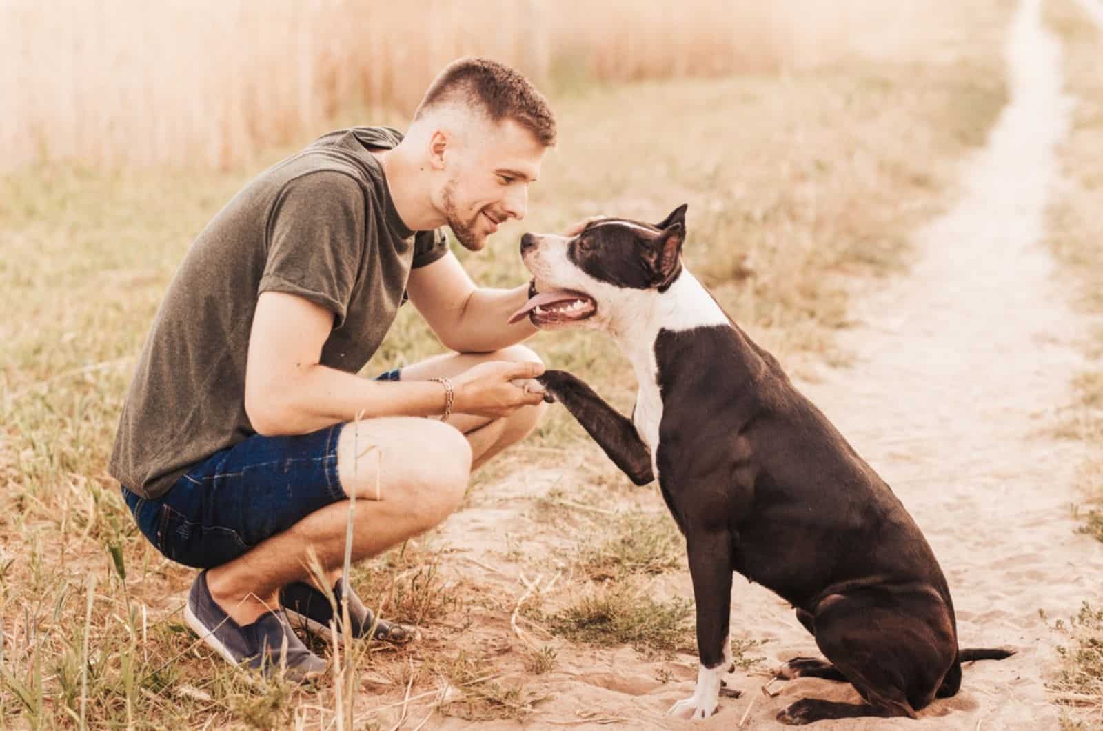 a man holding the paw of his pitbull in nature