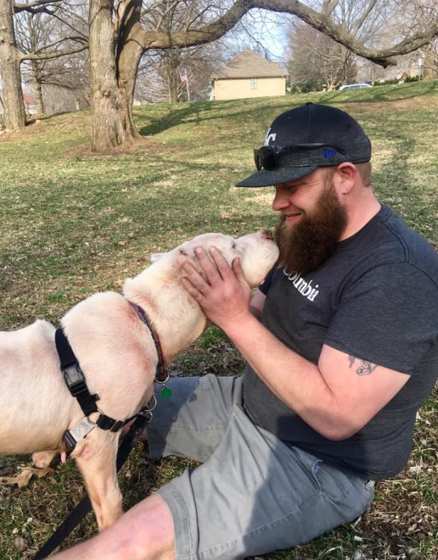 a man is sitting in an autumn park on the grass and petting a dog