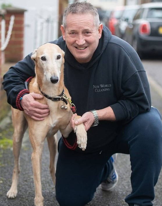 a man takes a picture with his dog, whose front paw he is guarding