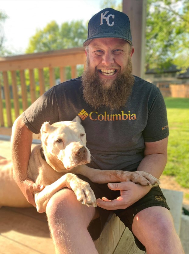 a smiling man is sitting on a wooden terrace and petting a dog