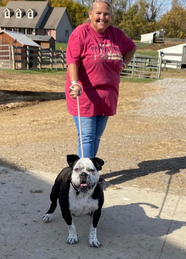 a smiling woman holds a dog on a leash