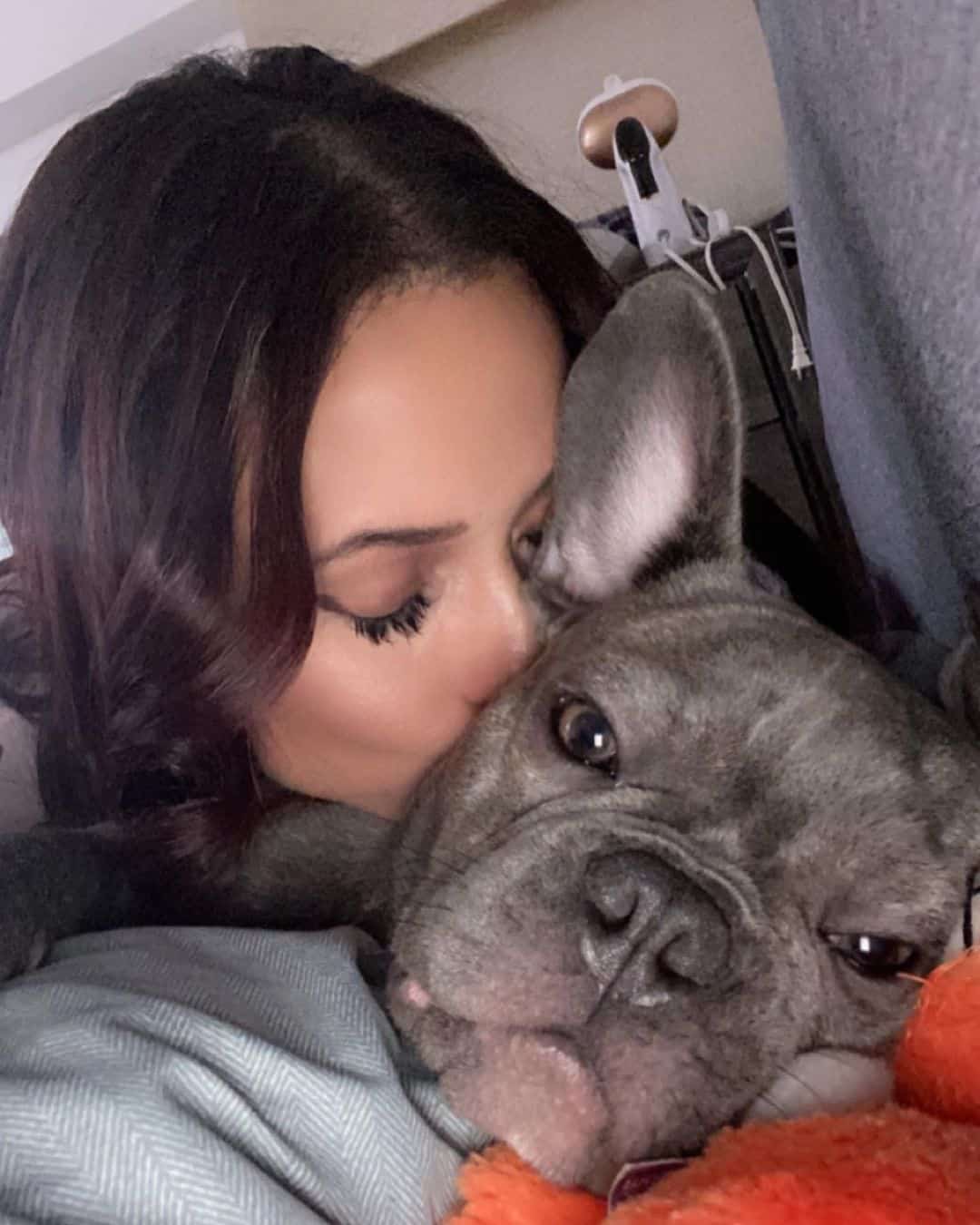 a woman kisses a blue french bulldog