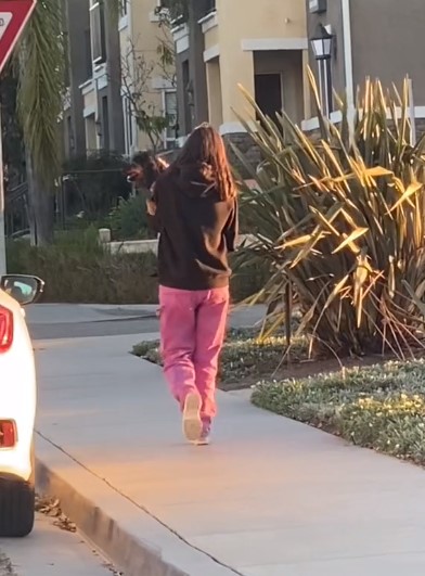 a woman walks down the street and carries a puppy in her arms