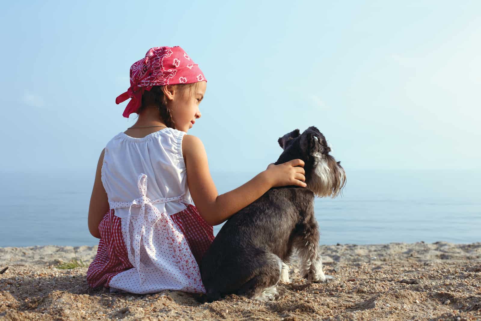 beautiful little girls embracing her dog looking at the sea