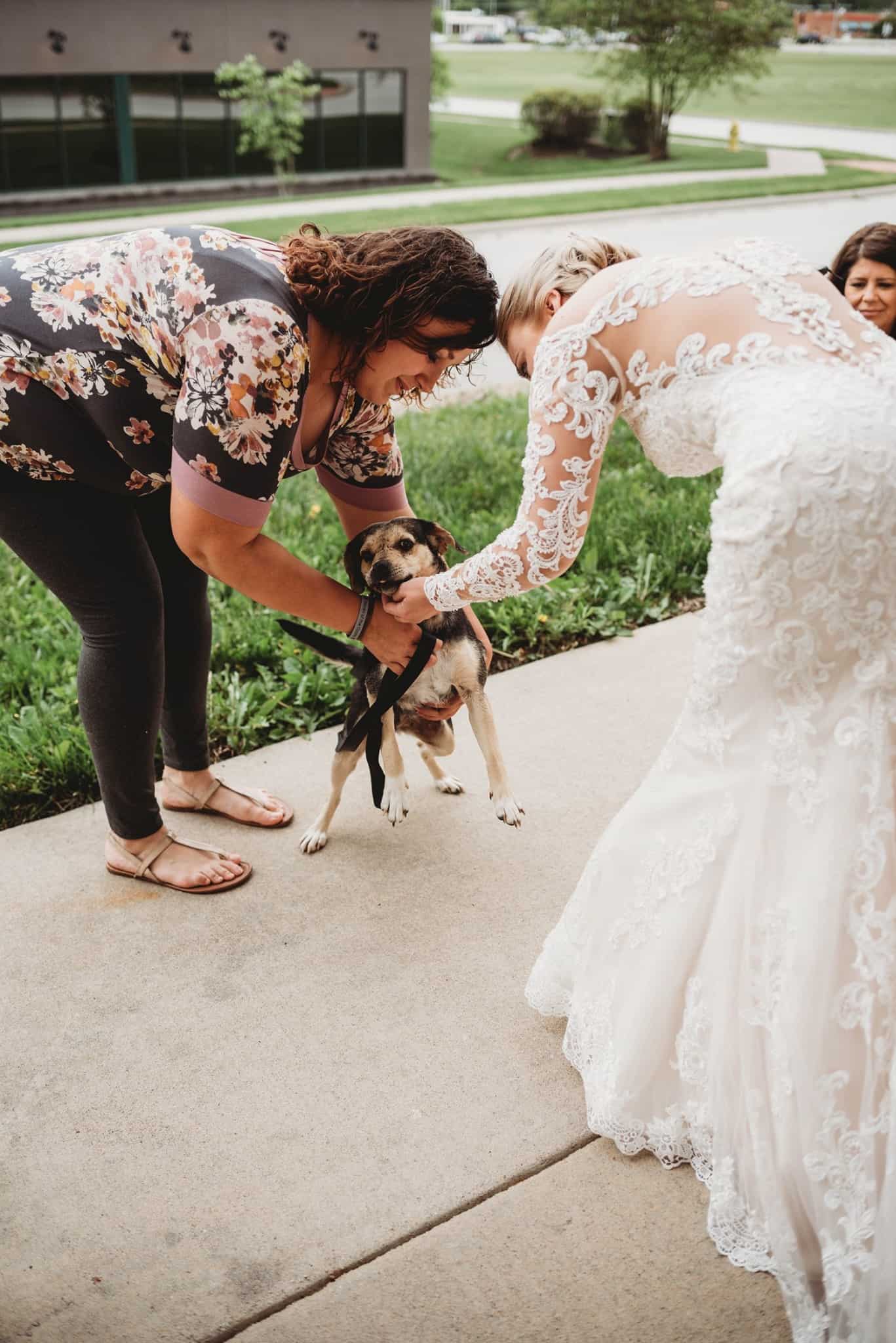bride cuddling a dog in front of house