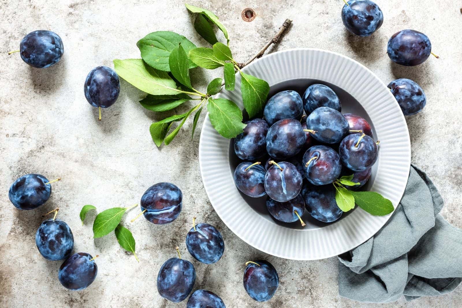 fresh plums on bowl with leaves on the table