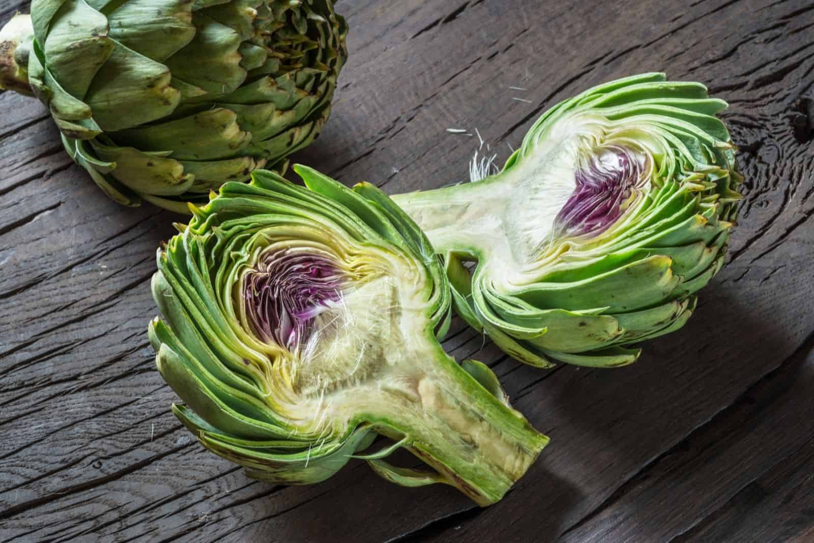 Green and purple artichoke flower edible buds on wooden background.