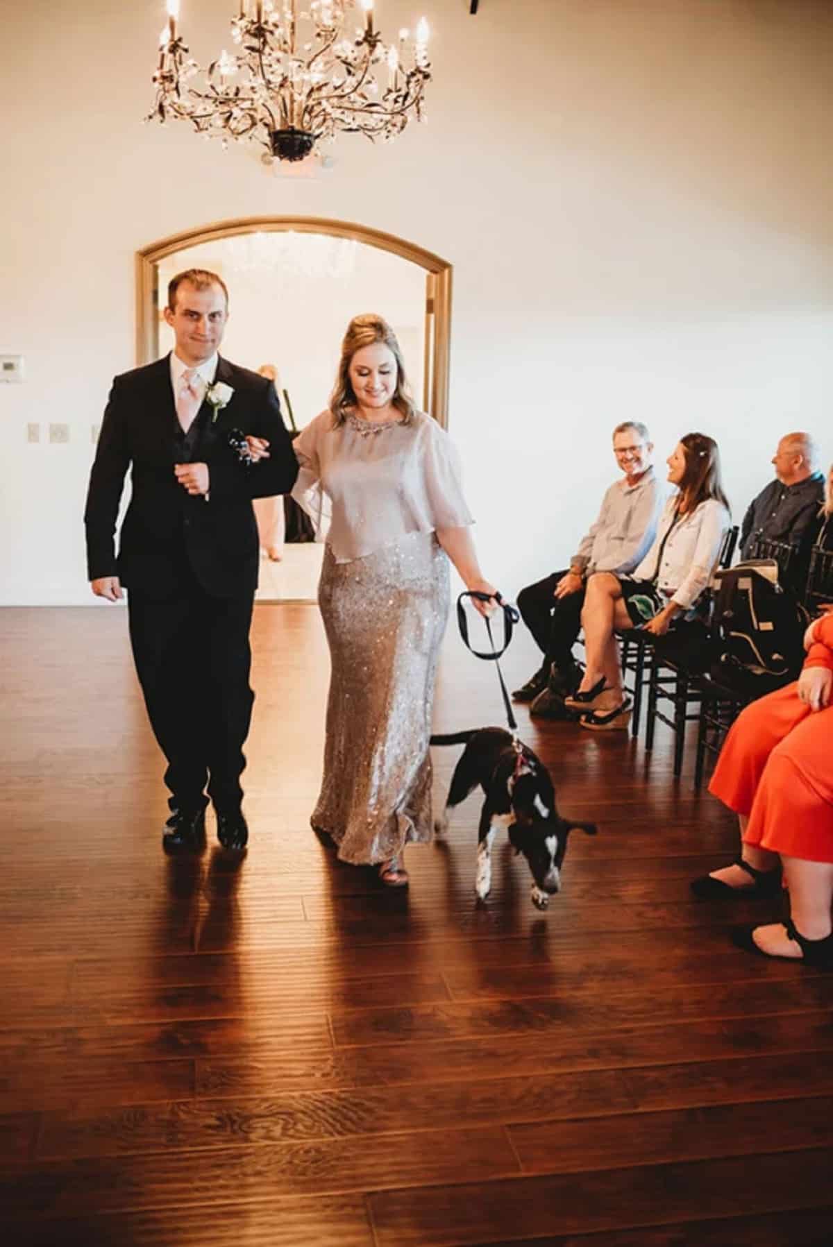 groom and bride holding dog on a leash