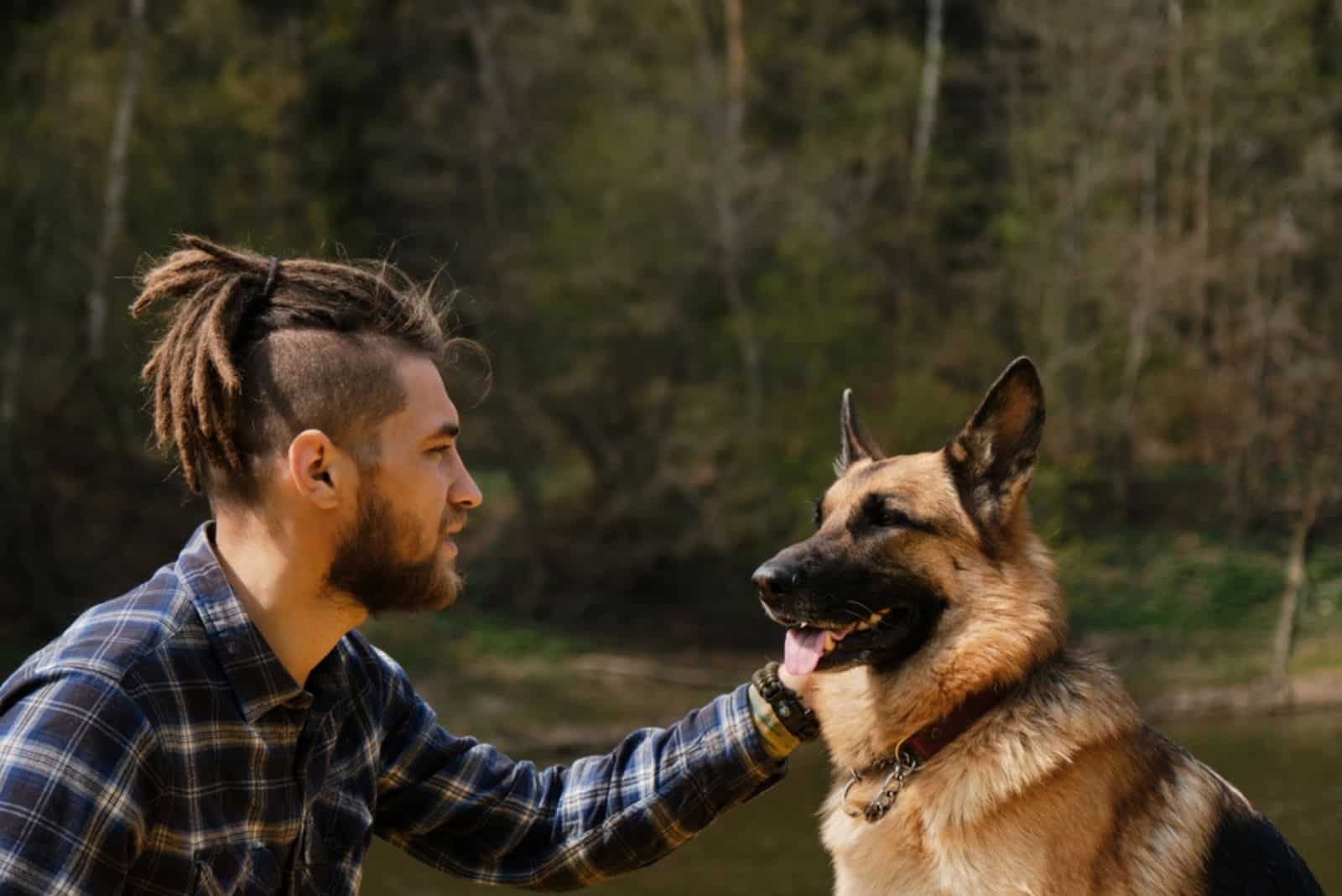 man cuddling german shepherd dog in nature