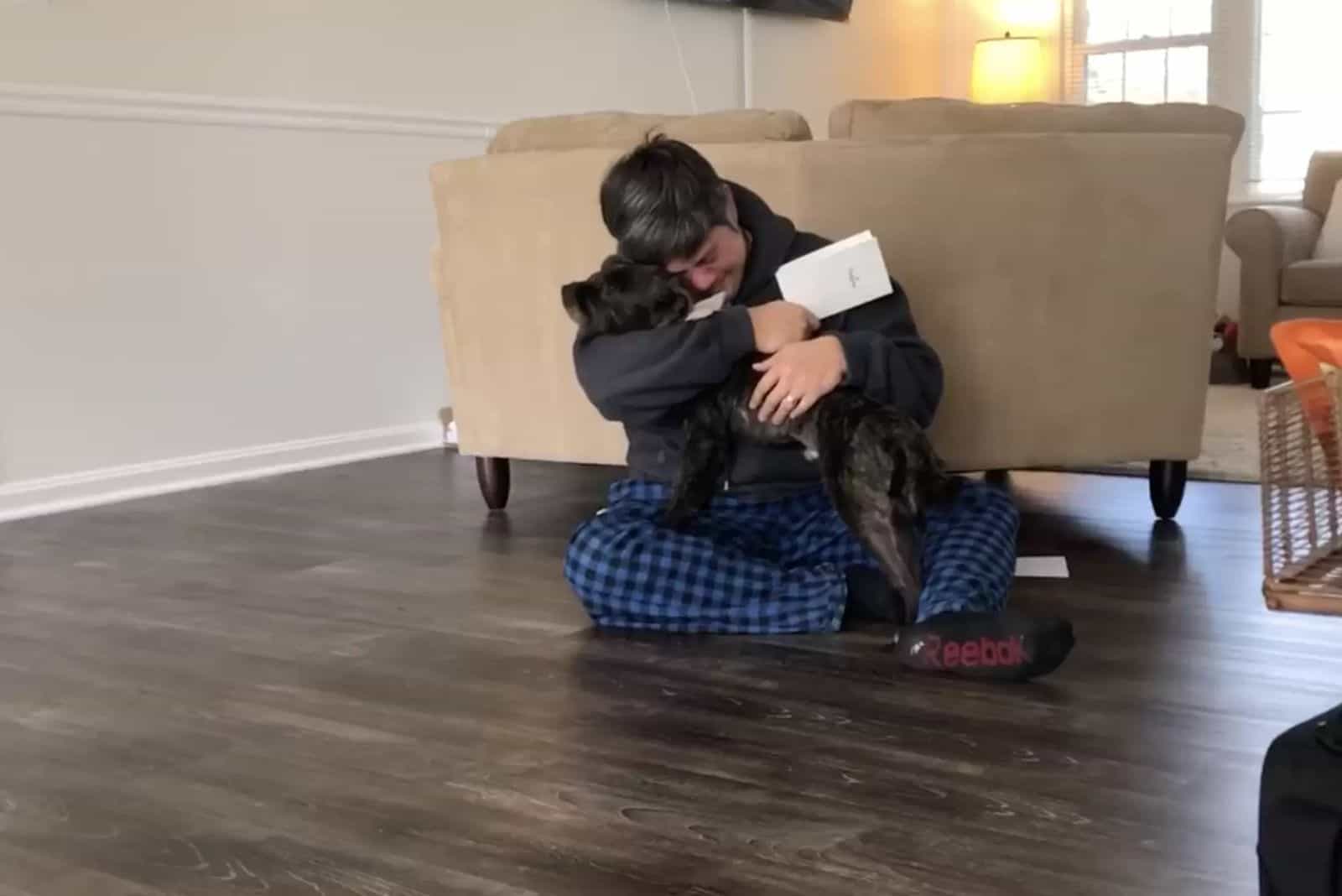 man embracing a black dog while sitting on the floor in living room