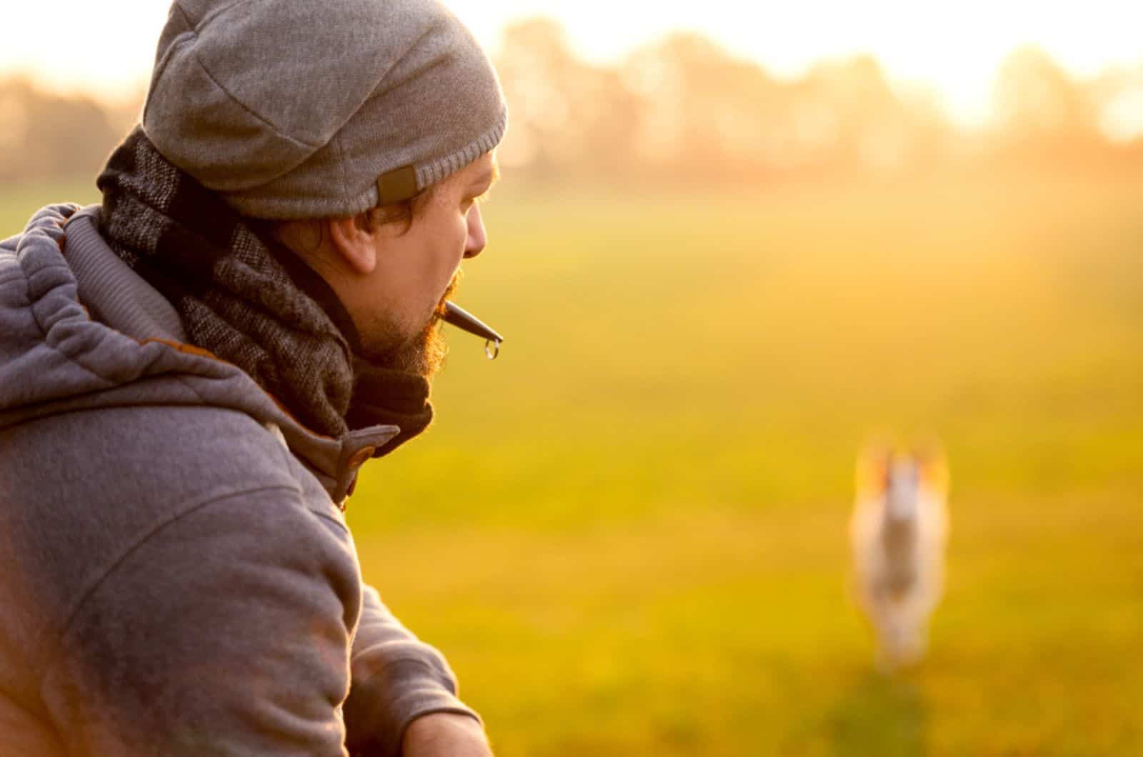 man is recall his dog with a dog whistle during training