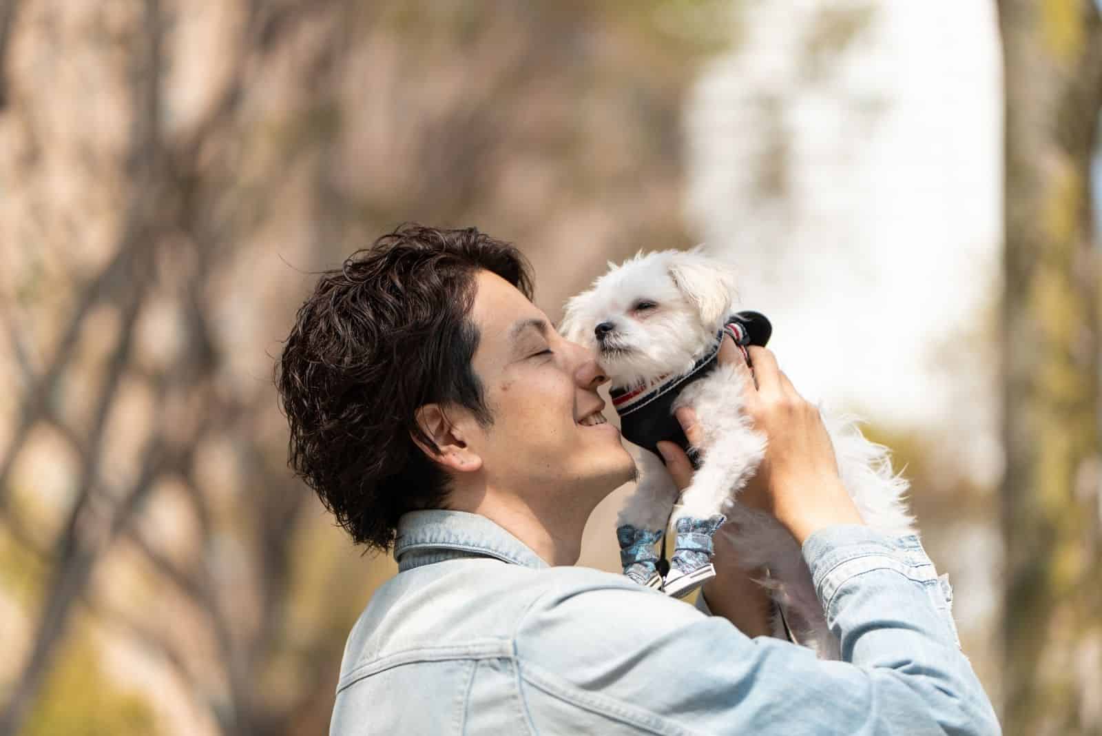 man lifting a puppy and placing it close to his face