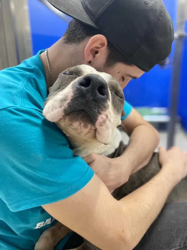 owner with hat hugging dog