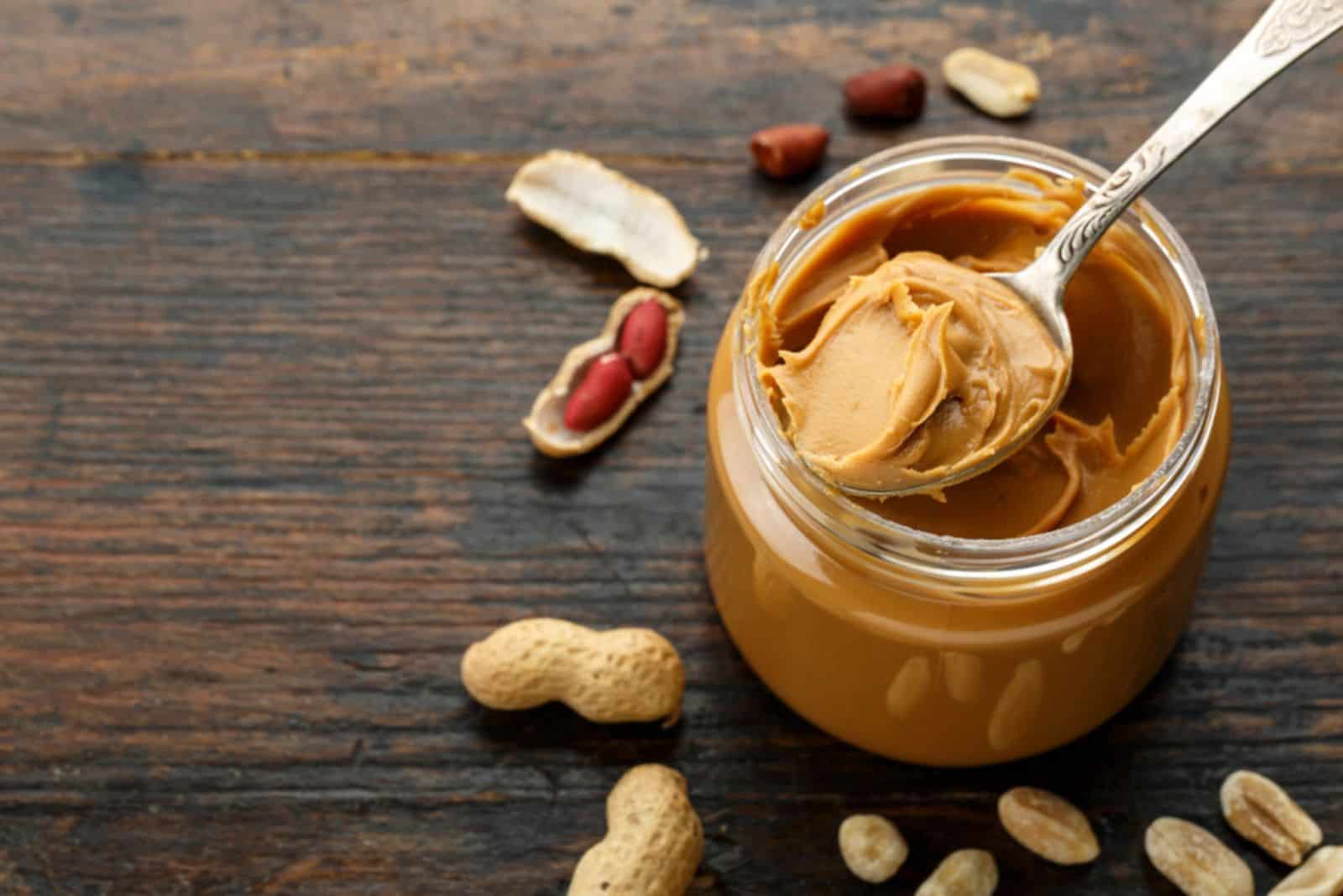 peanut paste in an open jar and peanuts in the peel scattered on the table