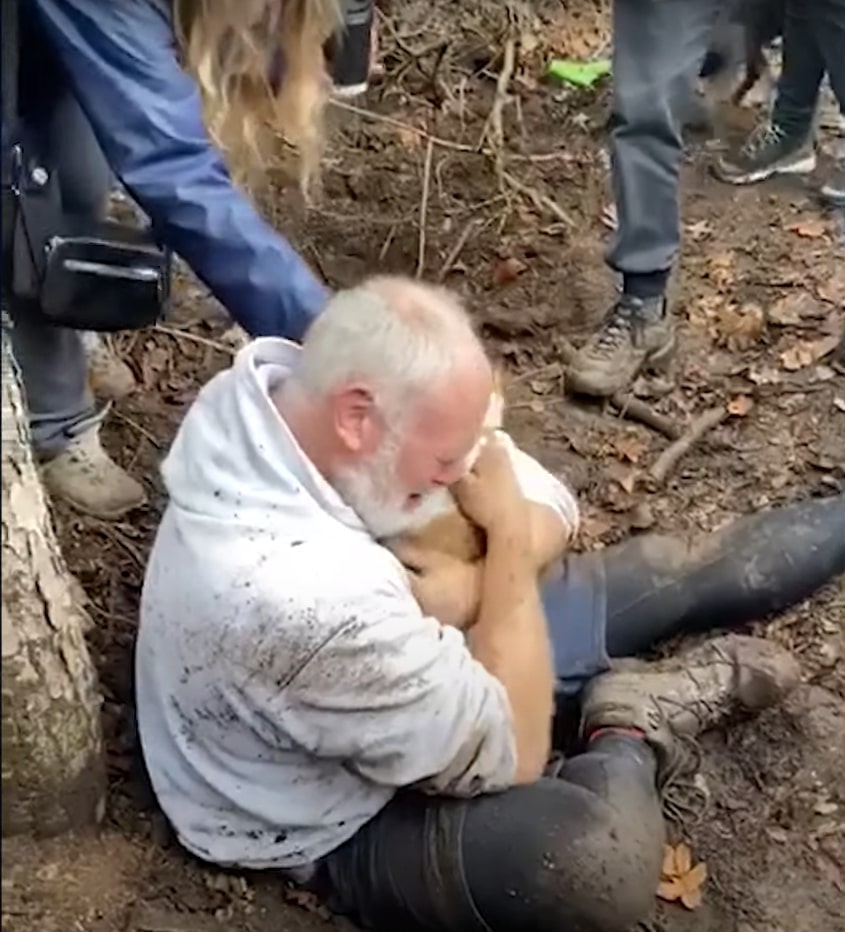 photo of man sitting on the ground and holding his dog