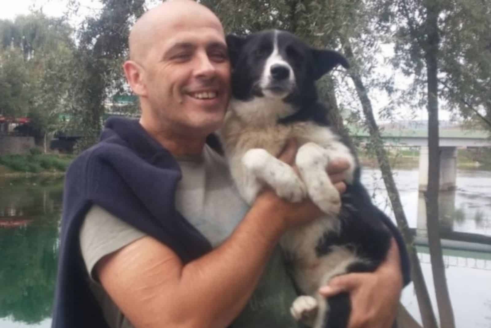 smiling man holding dog in his arms outdoors