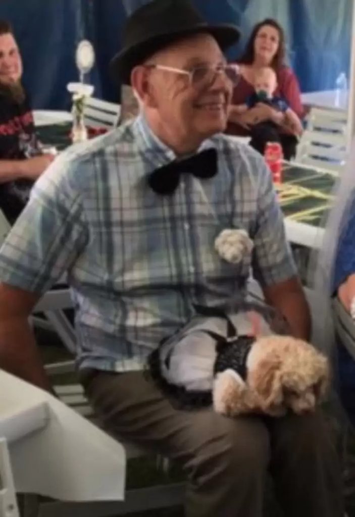 the dog is sitting on the grandfather's lap on the chair