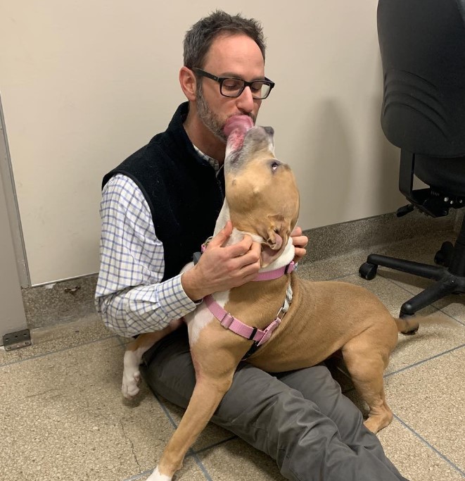 the man is sitting on the tiles, the dog is kissing her