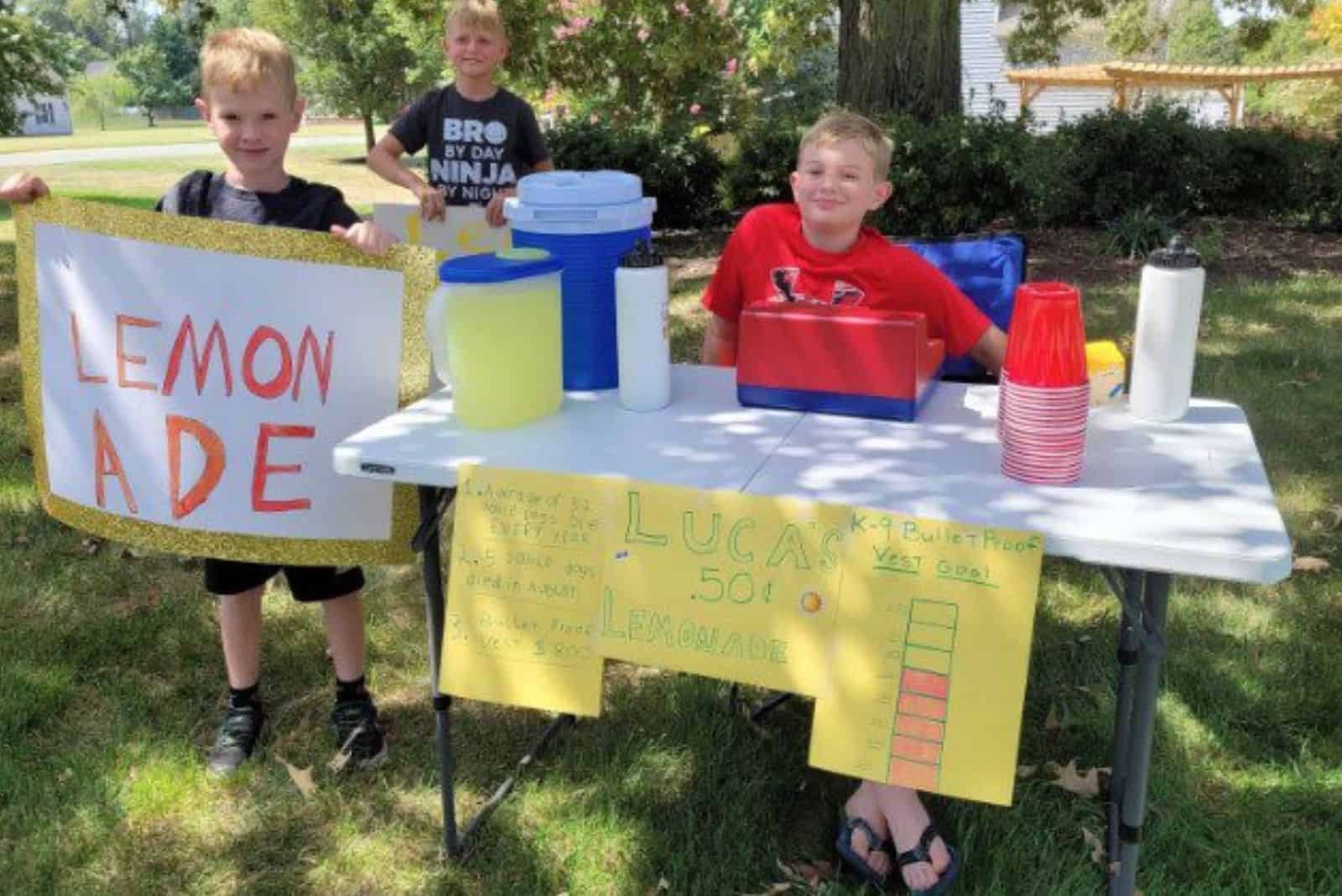 three boys are selling lemonade at a stand