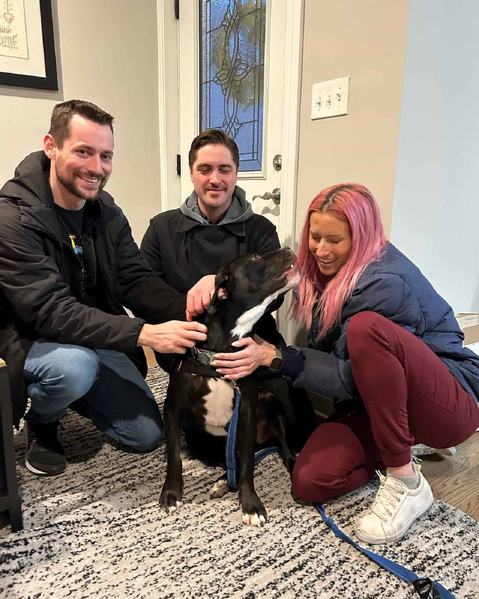 two men and a woman cuddling a dog in house