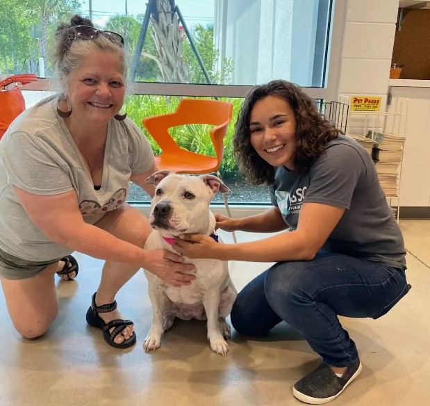 two smiling women take a picture with a white dog