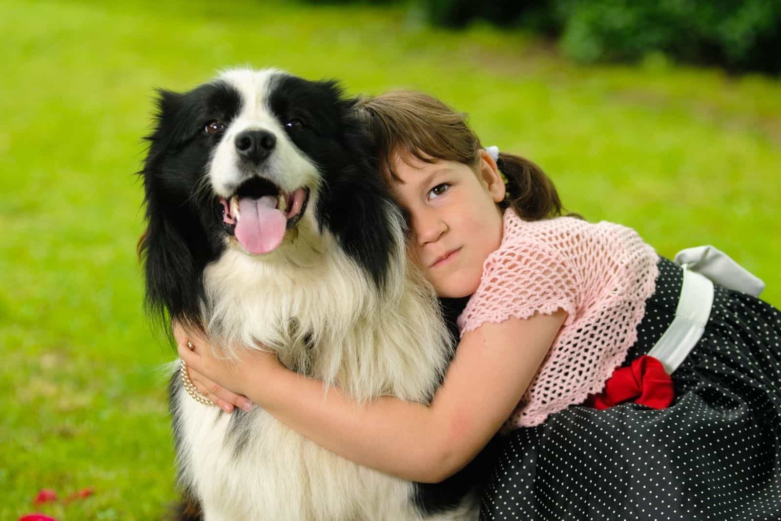 vintage dressed little girl hugging a border collie in the garden