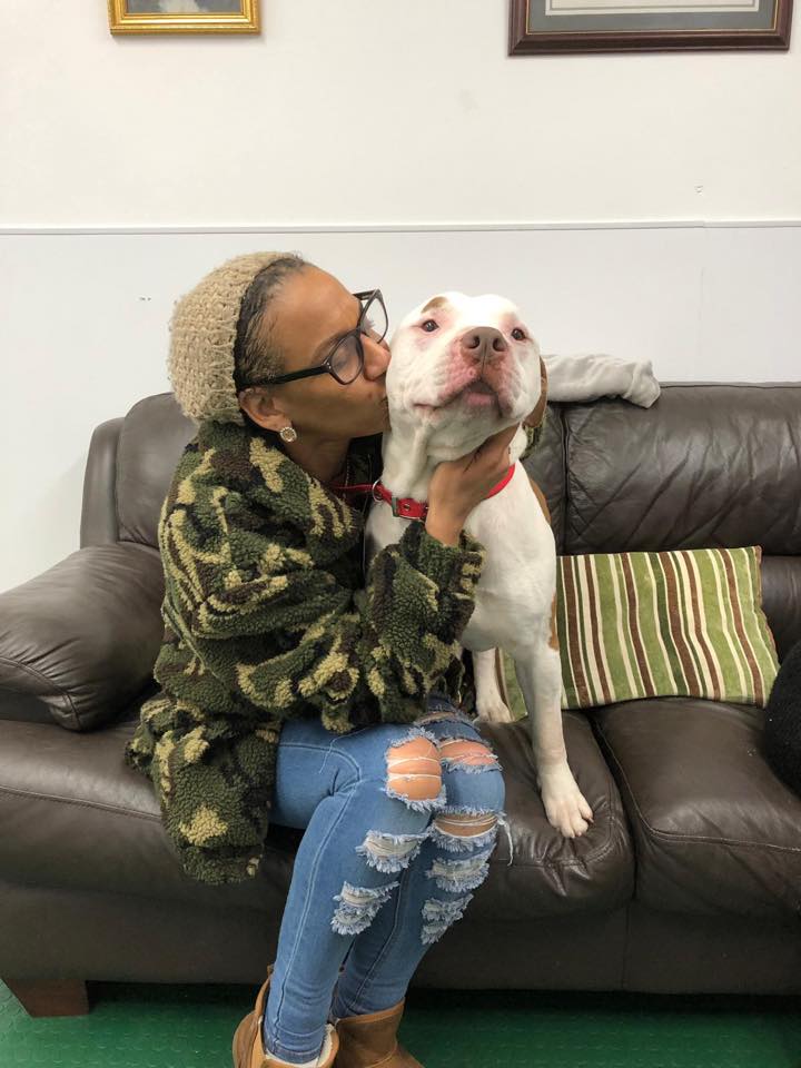 woman sitting on a couch with a dog and giving him a kiss