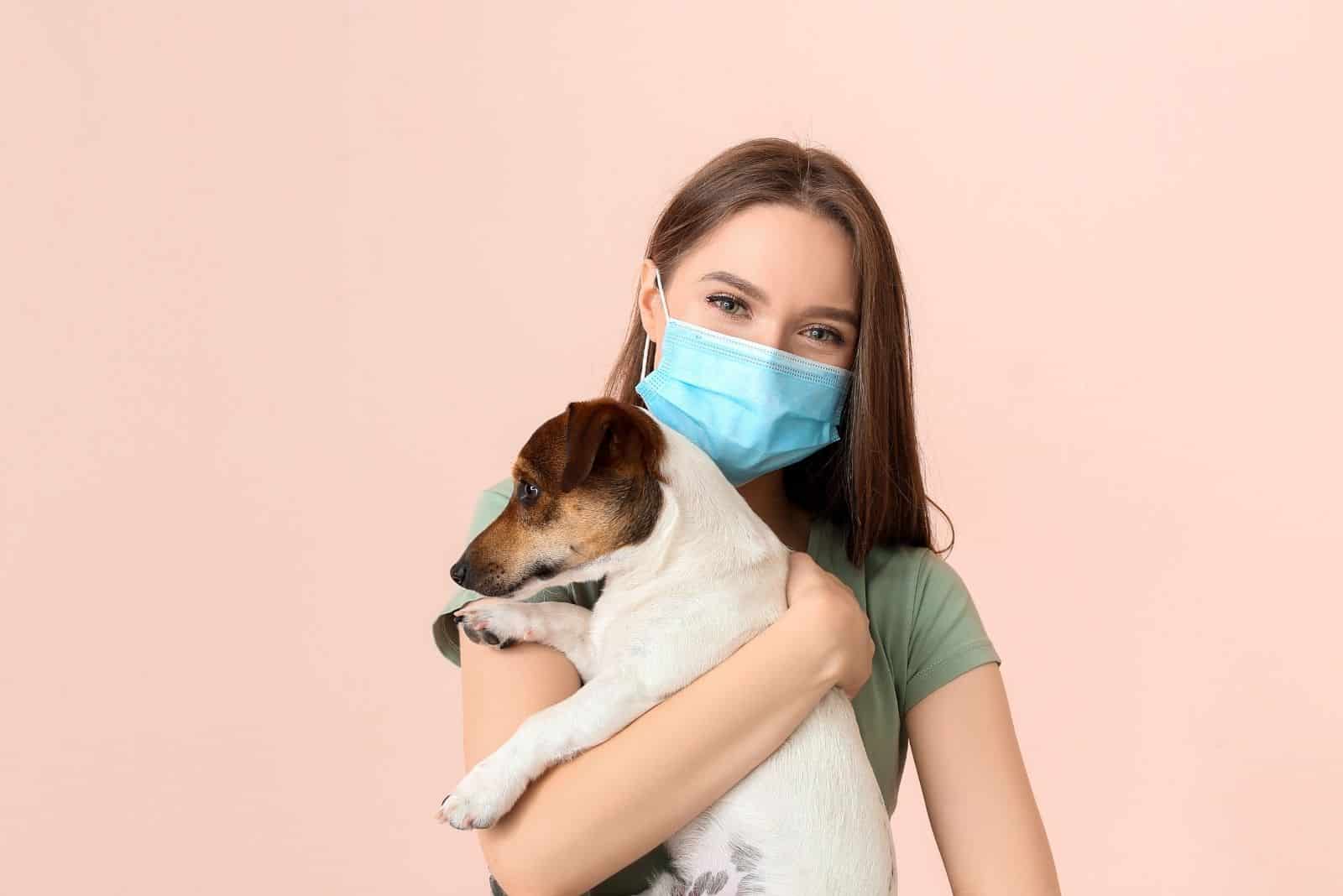 woman with a face mask hugging a dog in pink background