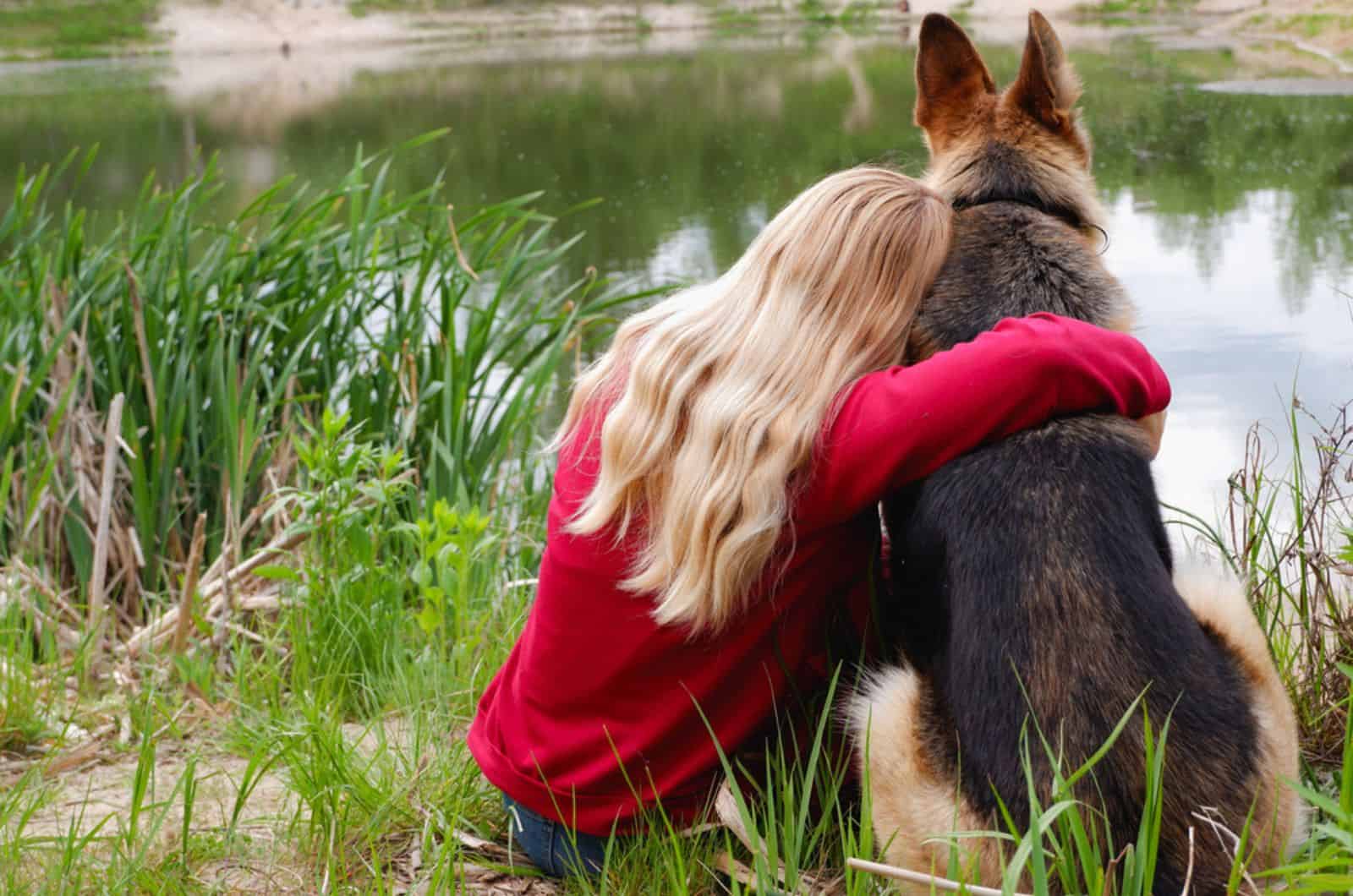 woman with a grerman shepherd dog sits on the shore of the lake