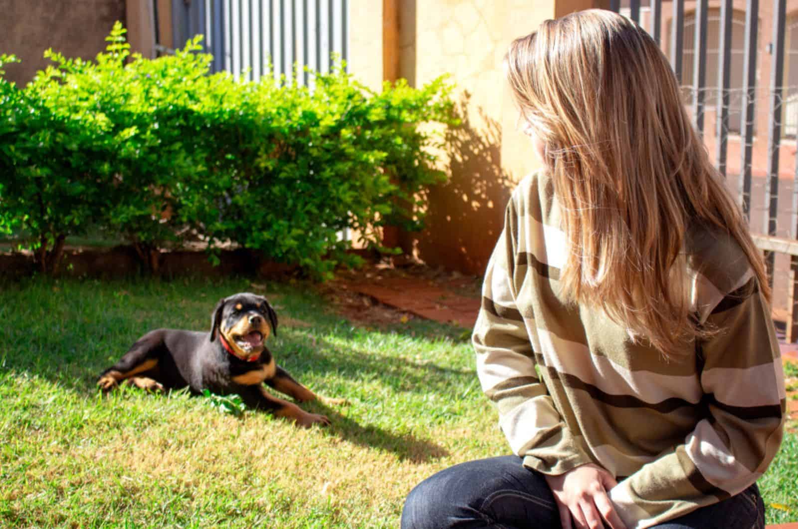 young woman sitting and looking to her rottweiler puppy in the garden