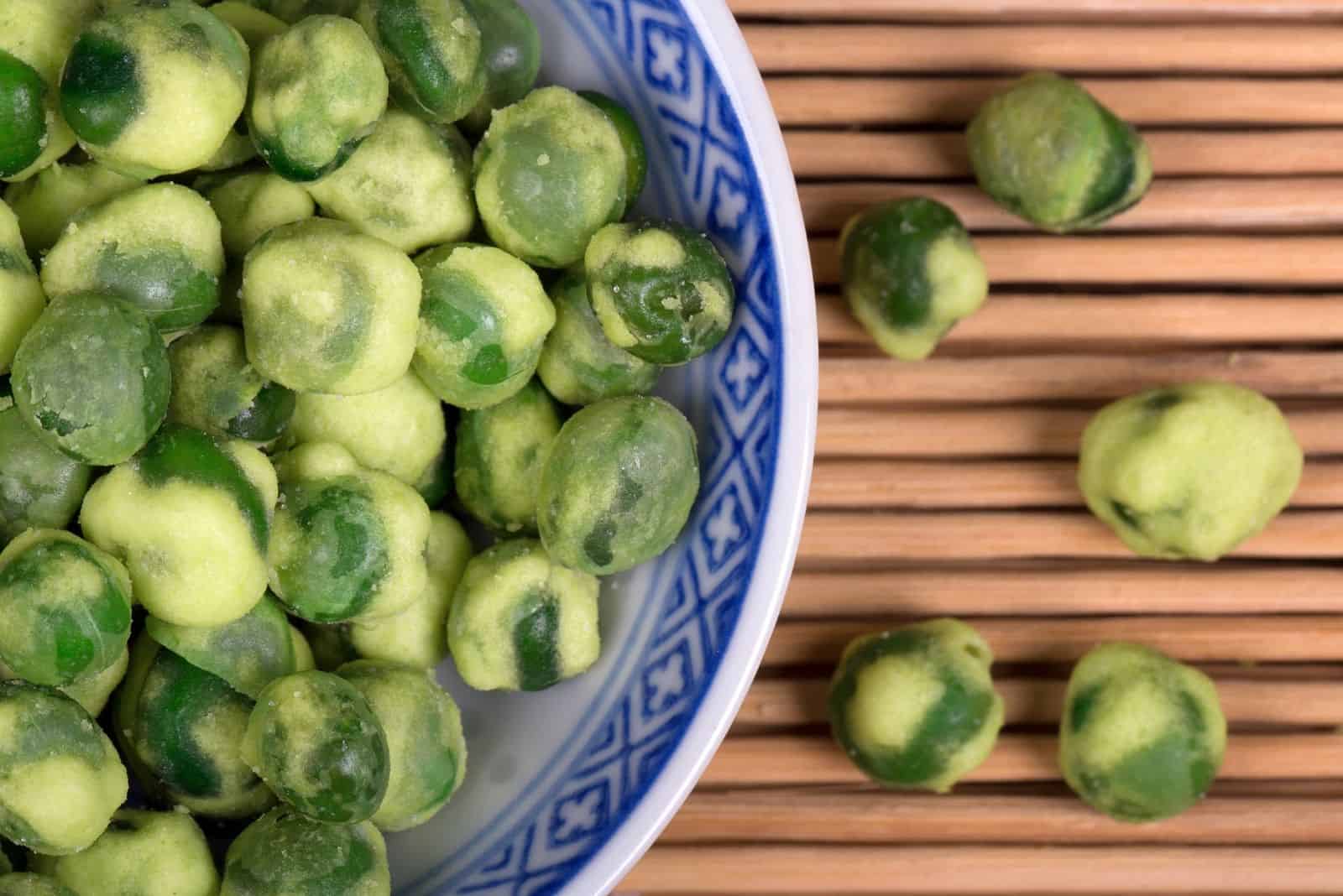 close up of wasabi peas in traditional white and blue porcelain bowl placed on bamboo mat