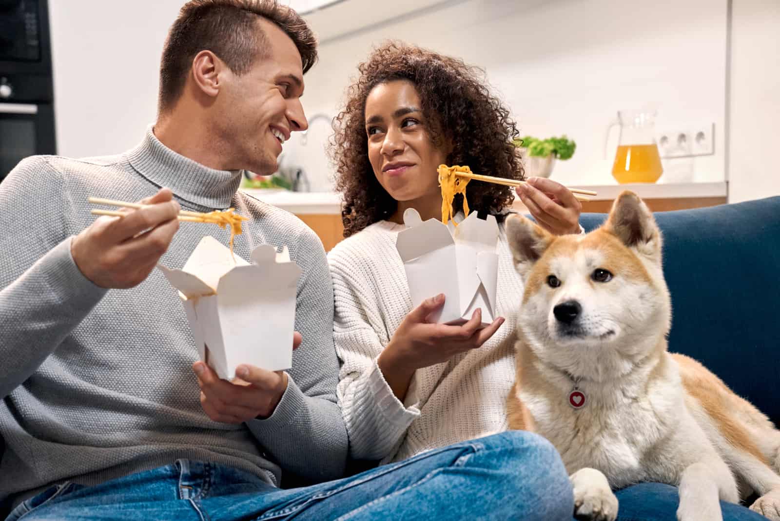 couple wearing sweaters having romantic date at home sitting on sofa at living room with akita inu dog