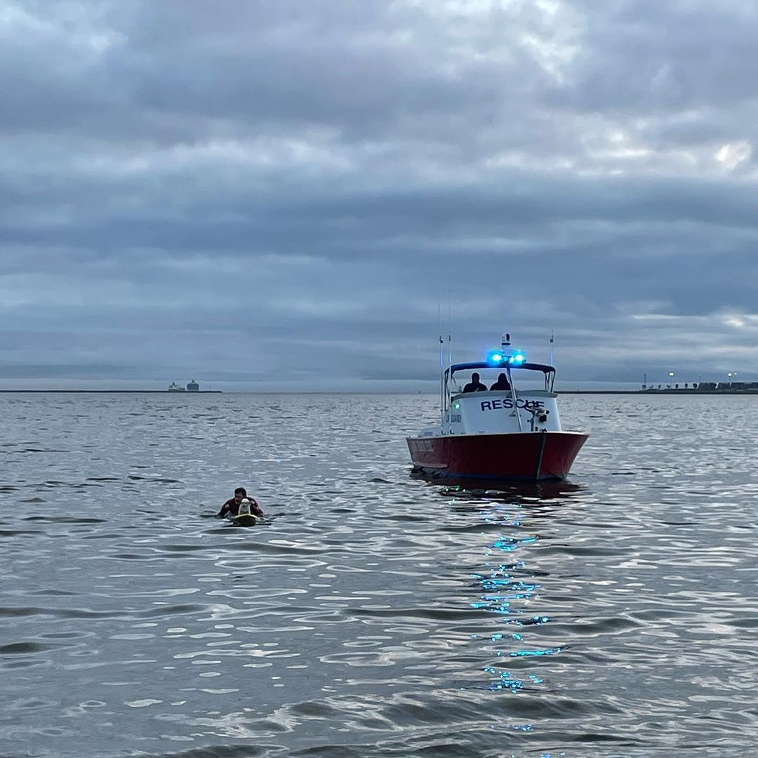 lifeguard on a paddle board next to a small boat in the ocean