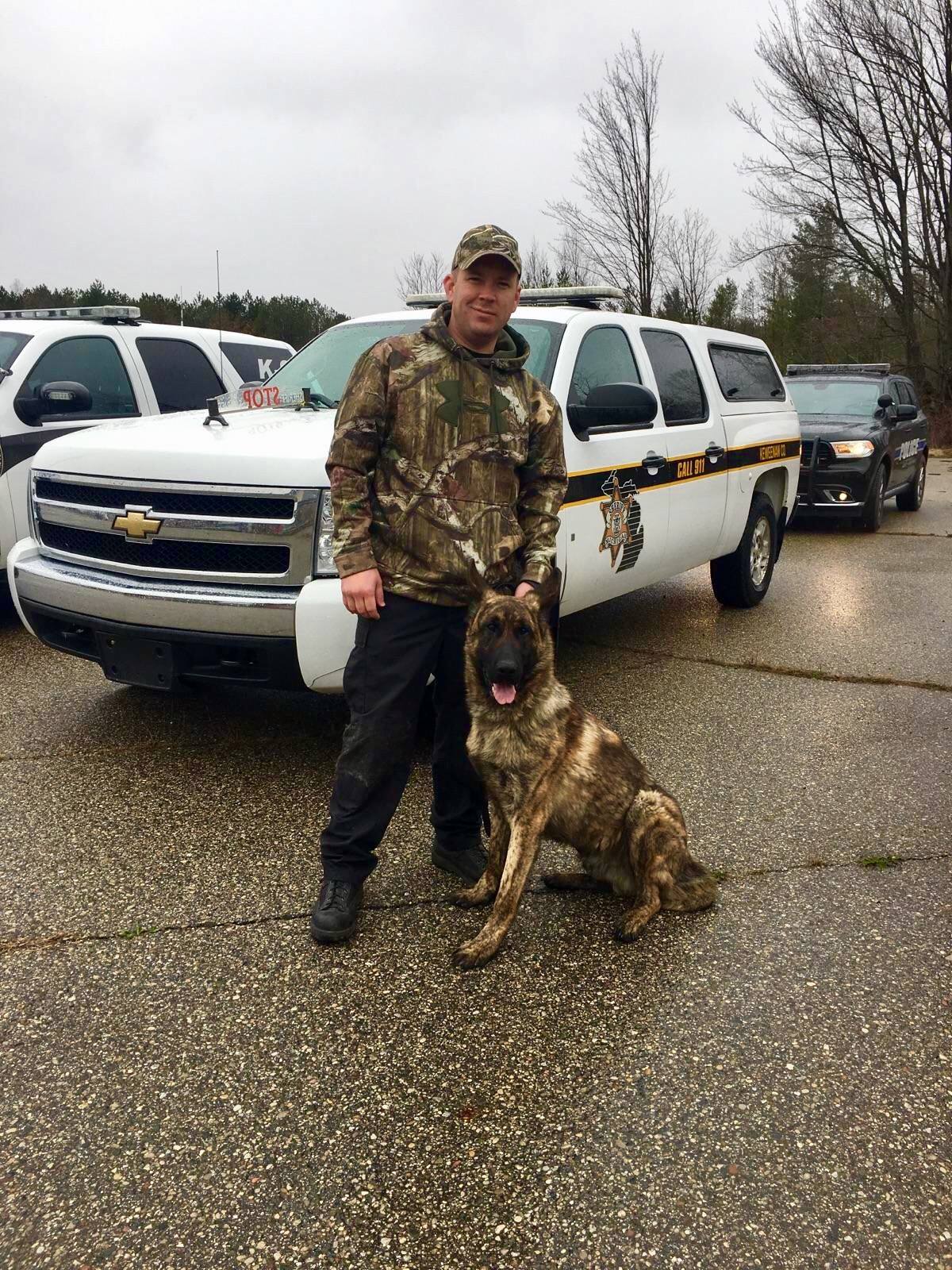 man posing with a K9 dog in front of a car