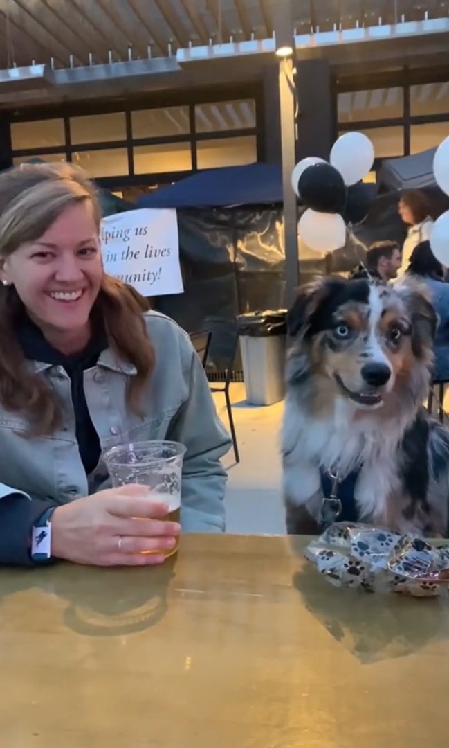 a smiling woman and a dog are sitting at the table